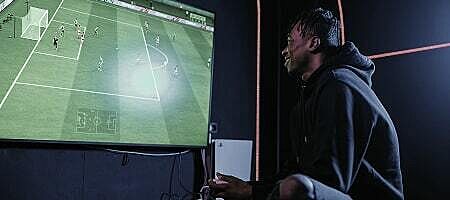 Junger Mann spielt ein Fußball-Videospiel auf einem großen Bildschirm – E-Sport und Gaming.
