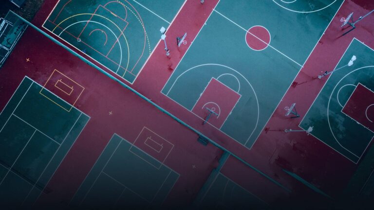 Luftaufnahme mehrerer farbiger Basketball- und Sportplätze in Rot- und Türkistönen von oben.