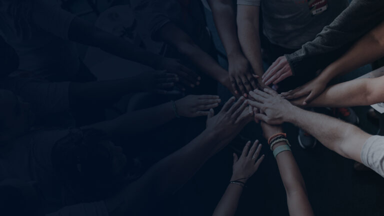 Viele Hände treffen sich in der Mitte eines Team-Kreises – Symbol für Gemeinschaft und Zusammenhalt.