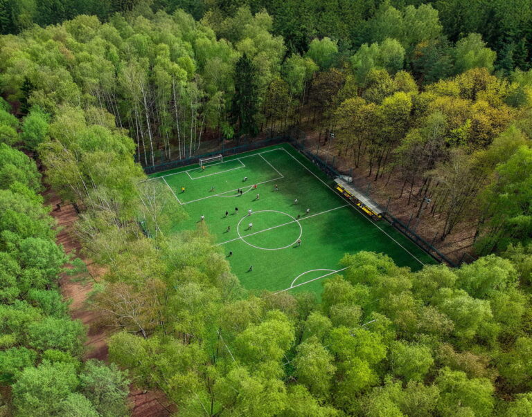 Fußballplatz mitten im grünen Wald mit Spielern auf dem Rasen, aus der Vogelperspektive.